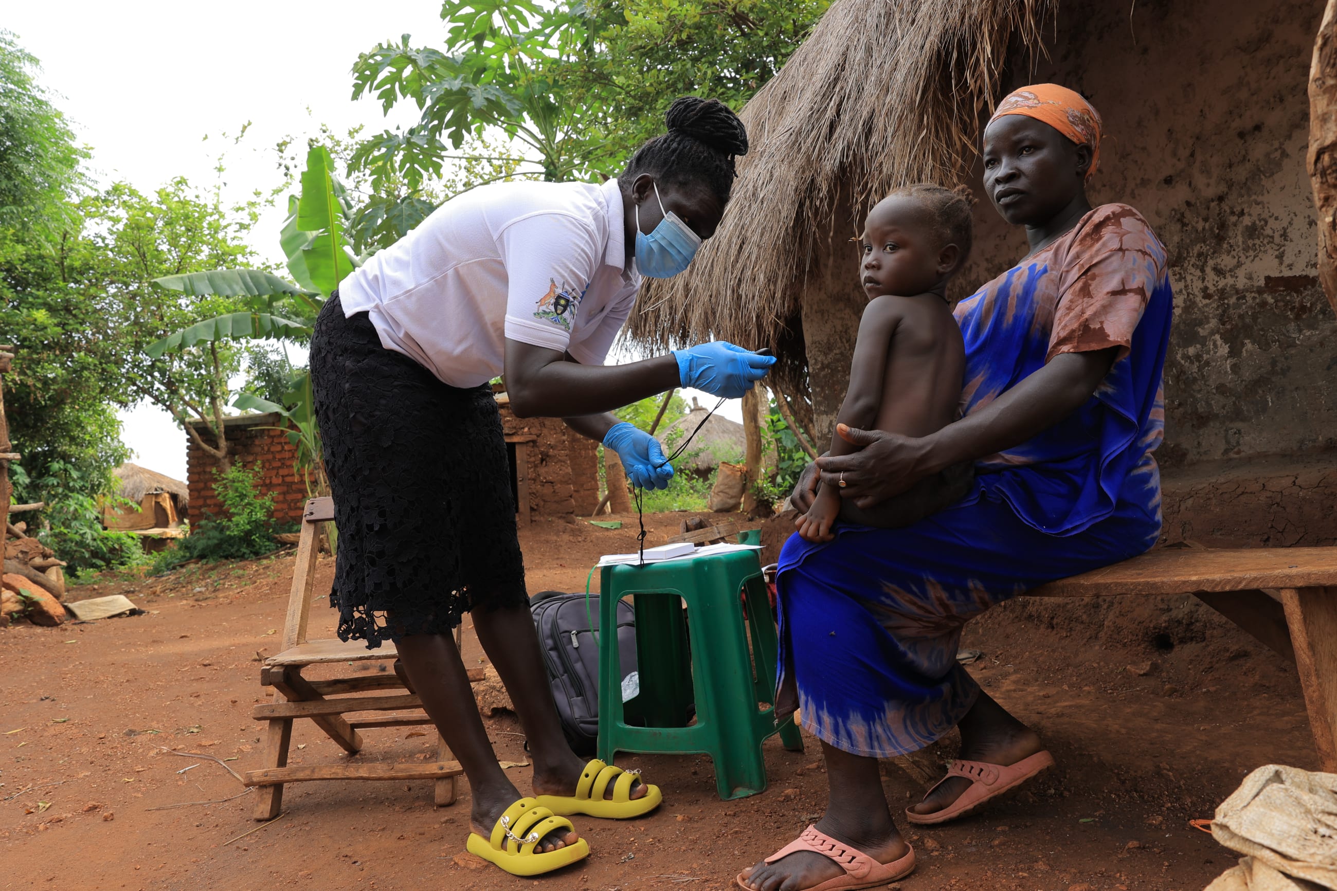 A community health worker examining a young child at a rural homestead