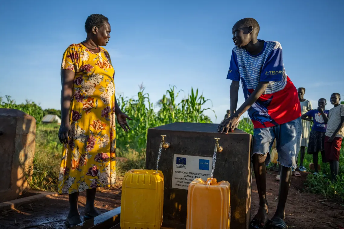A woman and a young man filling jerrycans at a community tapstand